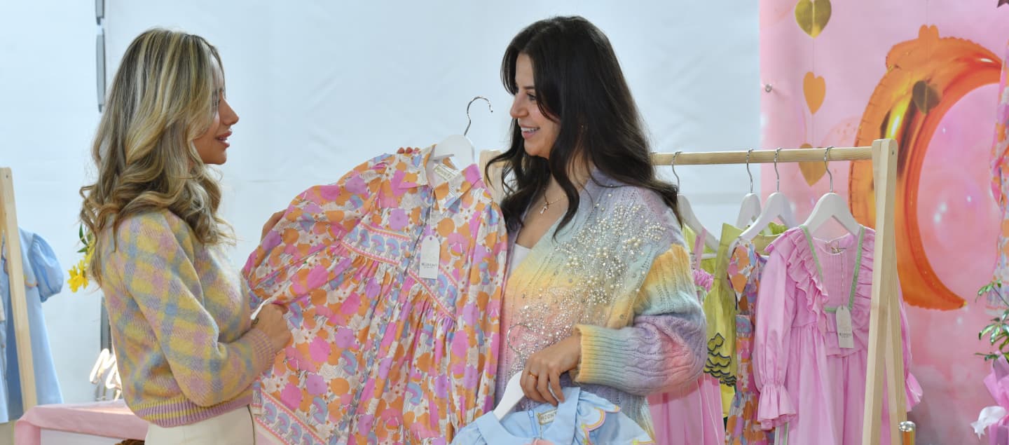 An exhibitor presenting a floral-patterned baby girl dress to a visitor at CBME Türkiye.