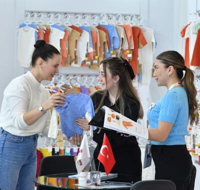 Three people discussing a blue garment at CBME Türkiye exhibition.