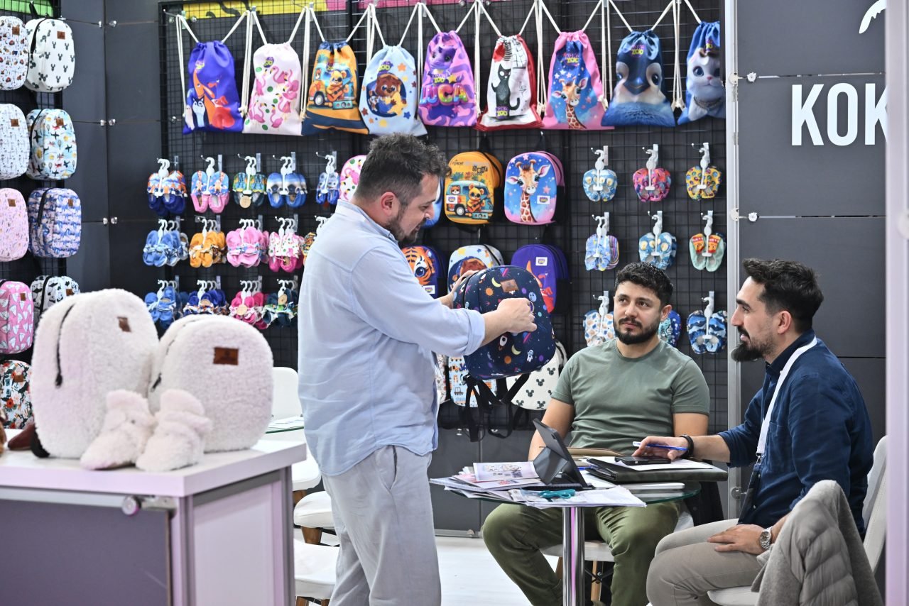 Three people discussing a blue garment at CBME Türkiye exhibition.