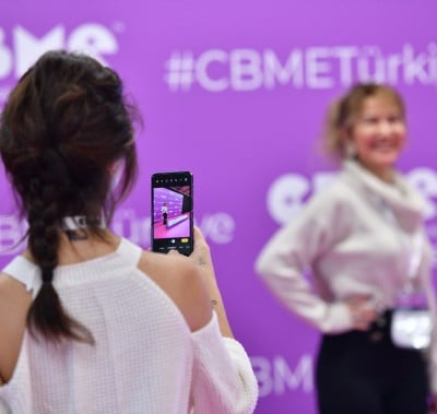 Person taking a photo in front of a promotional banner at CBME Türkiye.