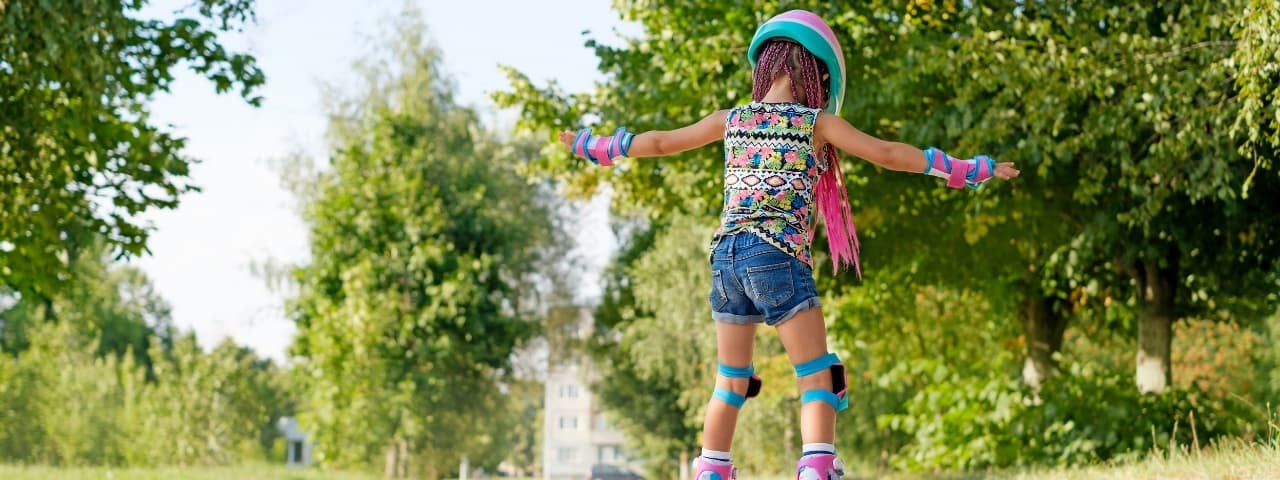 A girl wearing vibrant clothing skating in a park.