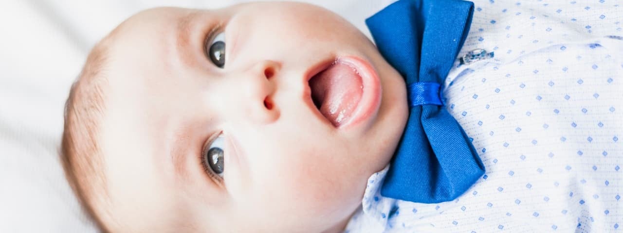 A baby lying down with an open mouth, wearing a bow tie, blue suspenders, and a polka-dot shirt.