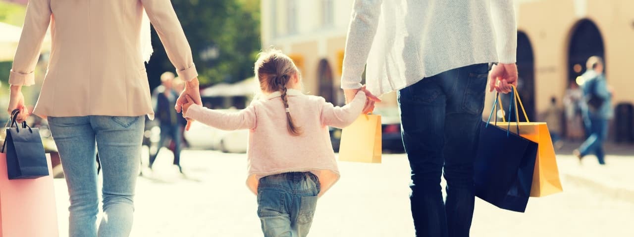 A young girl walking on the street, holding hands with her parents.
