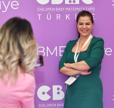 Woman from finance team smiling at CBME Türkiye exhibition with a #HeartOfTrade sign