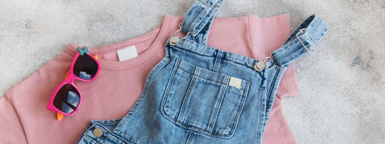 Çocuk kıyafetleri: kot tulum, pembe sweatshirt ve pembe güneş gözlüğü.
