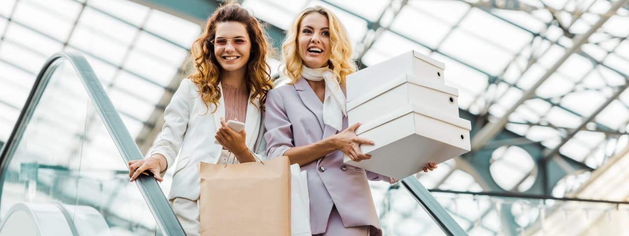 Yürüyen merdivende alışveriş çantaları ve kutular taşıyan iki kız.