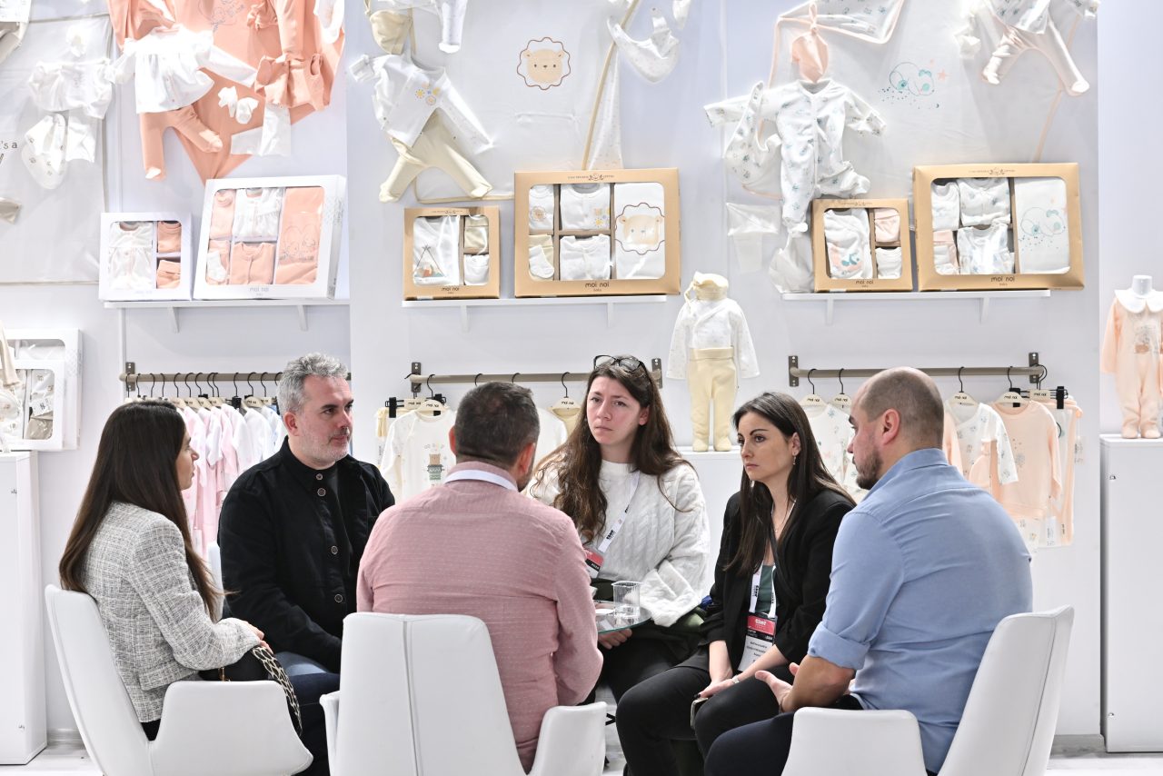 Three people discussing a blue garment at CBME Türkiye exhibition.