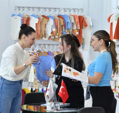 Three people discussing a blue garment at CBME Türkiye exhibition.
